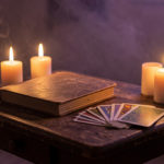 Table en bois avec plusieurs bougies allumées, des cartes posées et un carnet, dans une ambiance mystique douce et chaleureuse.